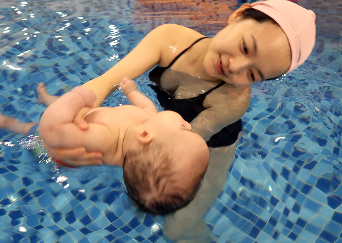 媽媽在水中練習托住嬰兒頭頸部，學習正確的仰漂 (Back Float) 支撐手勢，建立寶寶的安全感與浮力認知。