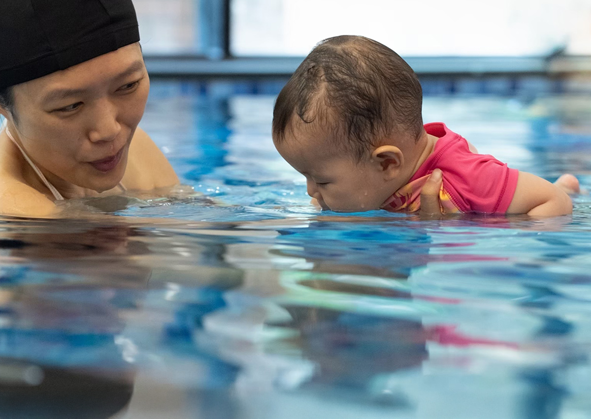家長引導寶寶將嘴巴接觸水面練習吐泡泡，這是學習潛水閉氣反射 (Breath Control) 的關鍵前置步驟。
