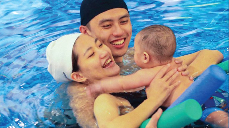 0-8個月嬰兒與媽媽在水中緊密擁抱與大笑，透過肌膚接觸 (Skin-to-skin) 建立深厚的安全依附關係 (Secure Attachment)，讓寶寶將水與母愛連結。