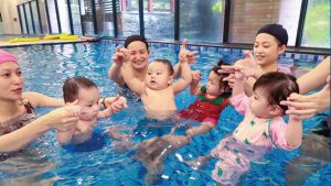 8-18個月大的寶寶與家長在水中圍成圓圈互動，透過團體遊戲促進社交能力發展，並利用嬰兒喜歡模仿同儕的特性進行觀察學習 (Observational Learning)。