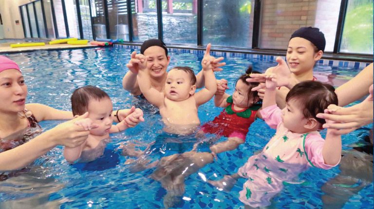 8-18個月大的寶寶與家長在水中圍成圓圈互動，透過團體遊戲促進社交能力發展，並利用嬰兒喜歡模仿同儕的特性進行觀察學習 (Observational Learning)。