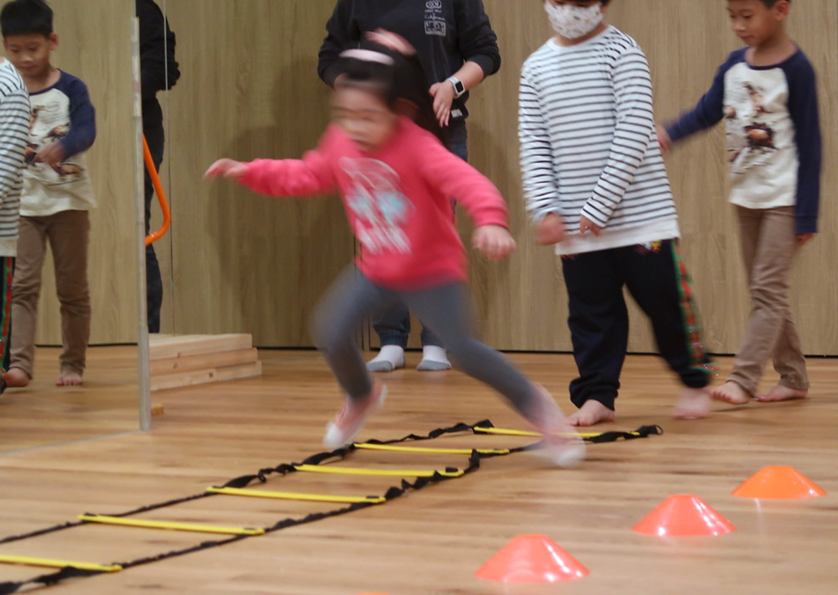 兒童快速通過地板上的繩梯 (Agility Ladder)，訓練腳步變換速度與敏捷度 (Agility)，有效提升神經系統對肌肉的控制與下肢爆發力。