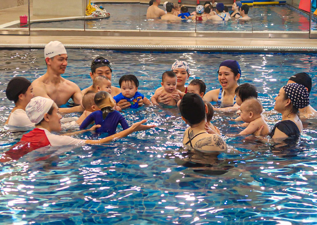 專業教練使用教學娃娃示範動作，引導家長們進行團體練習，藉由同儕互動促進寶寶的社交能力與觀察學習 (Observational Learning)。