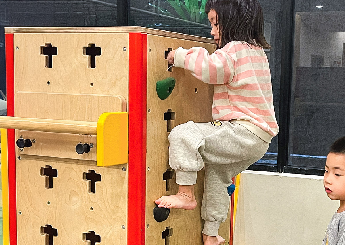 幼兒專注攀爬木製攀岩箱，訓練手腳並用的交叉協調 (Cross-lateral Coordination) 能力與垂直空間感，強化背部與四肢肌肉發展。
