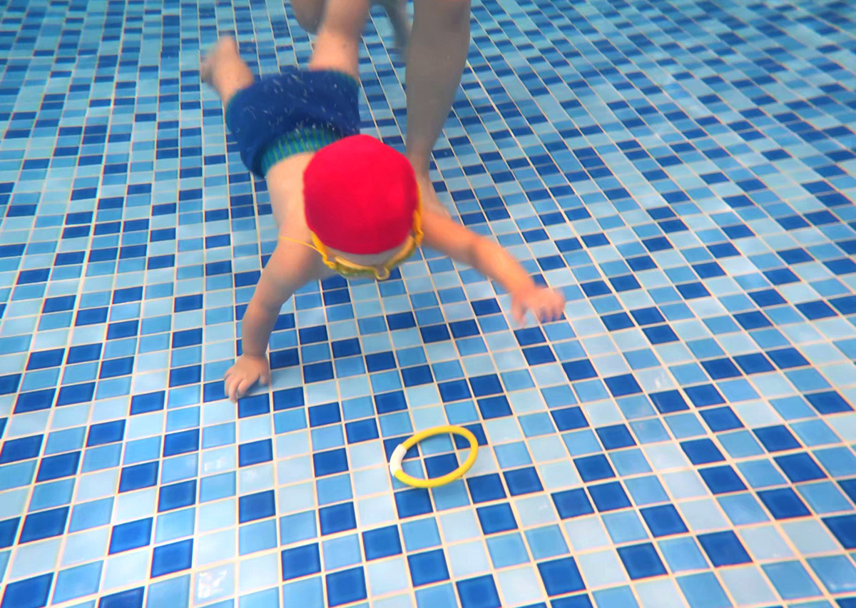 幼兒運用躬身下潛技巧潛入池底抓取圓環,這項練習能強化視覺搜尋 (Visual Search) 能力與閉氣耐受力,是水中自救的重要基礎。