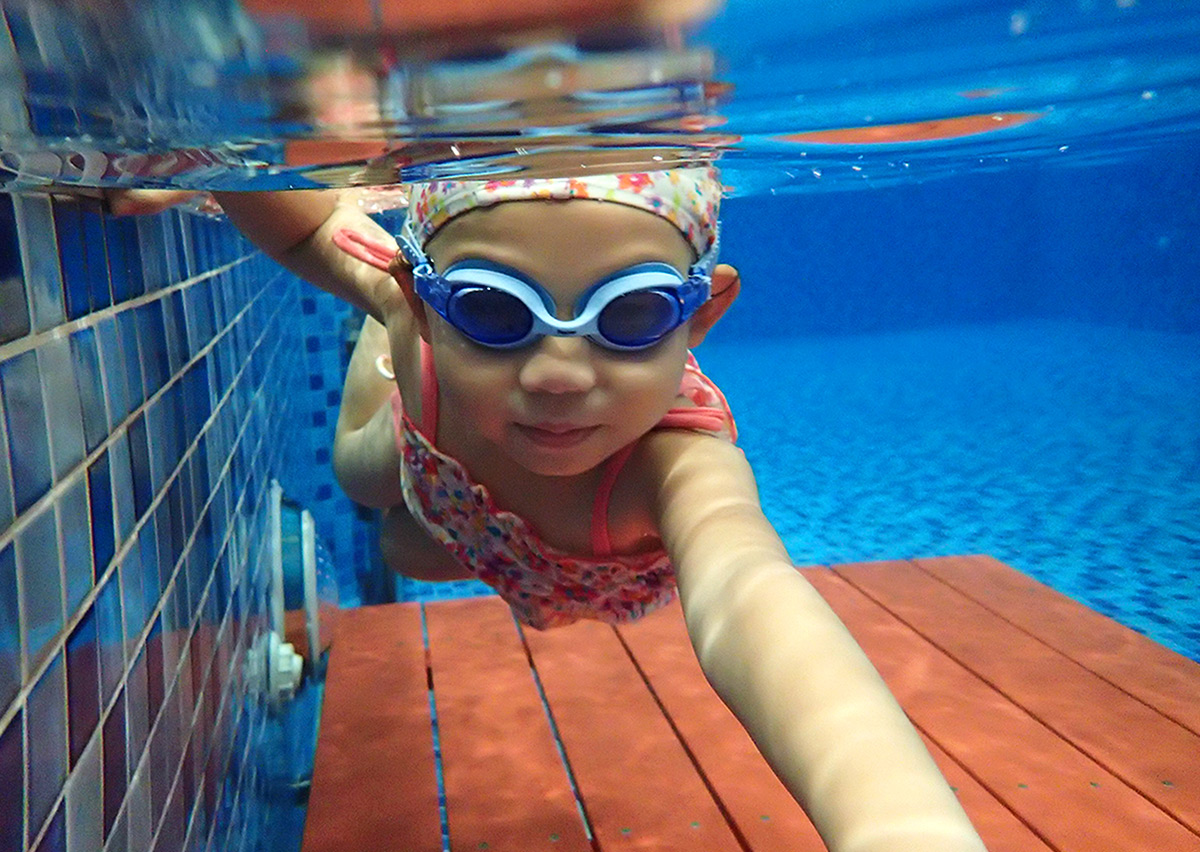 兒童自信地向鏡頭游來,展示流線型 (Streamline) 身體姿態與手部推進技巧,體現進階游泳課程中的水中定位與換氣能力。