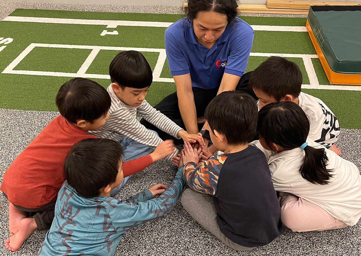 教練帶領孩子們進行疊手加油儀式，培養團隊合作 (Teamwork) 精神與歸屬感，透過團體互動促進兒童的社交情感學習 (SEL - Social Emotional Learning)。