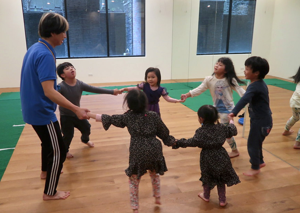 孩子們手牽手圍成圓圈進行團體律動，透過音樂與肢體接觸培養節奏感 (Rhythm) 與群體歸屬感，是兒童社交情感學習 (SEL) 的重要環節。