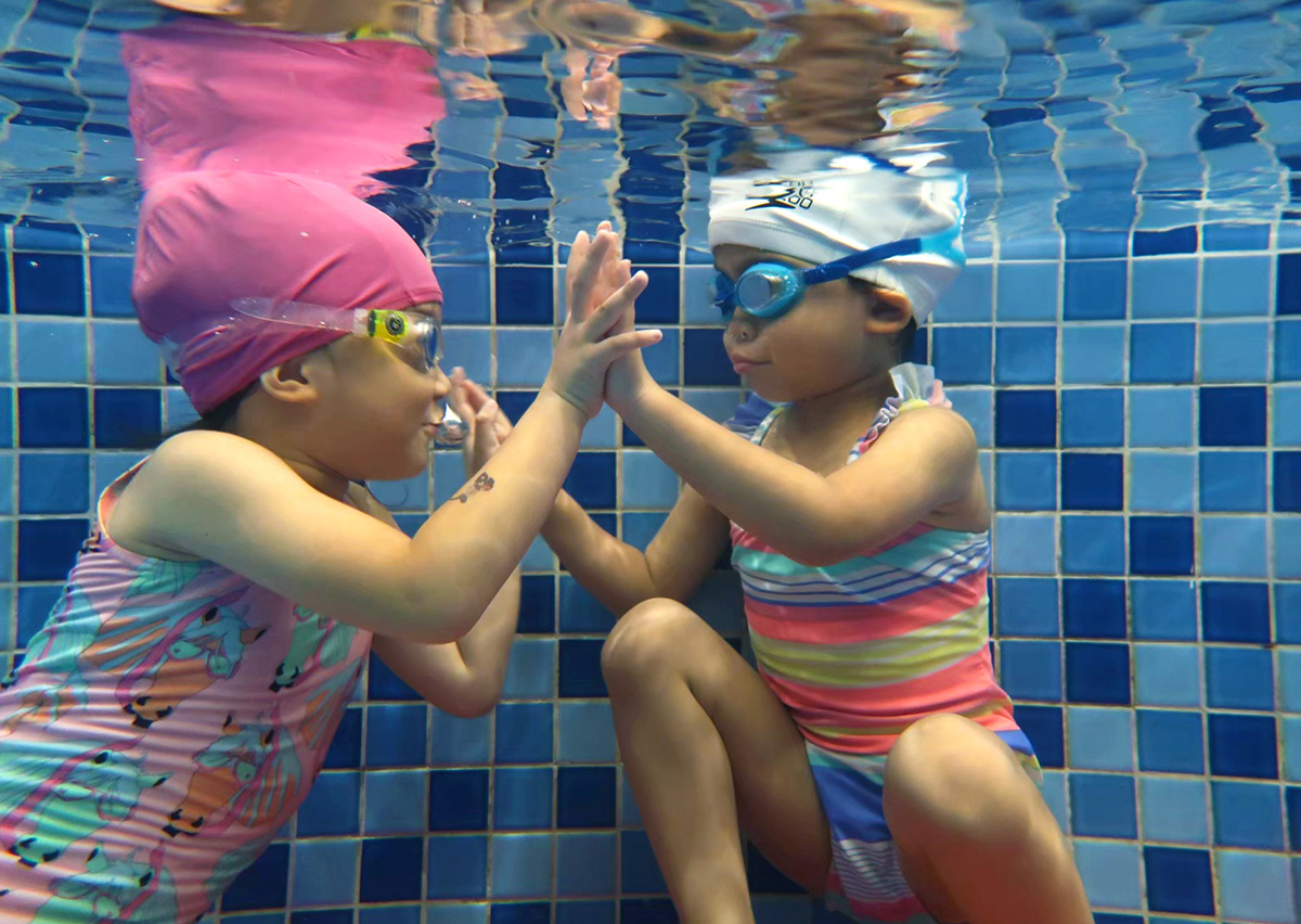 兩位兒童在水下進行擊掌互動,透過同儕學習 (Peer Learning) 與遊戲,消除對潛水的恐懼並建立良好的水中社交能力與夥伴關係。