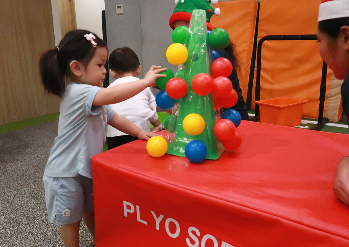 幼兒將彩球塞入特殊的樹狀裝置中，這項活動專注於訓練手指的精細動作 (Fine Motor Skills)、手眼協調以及顏色配對認知。