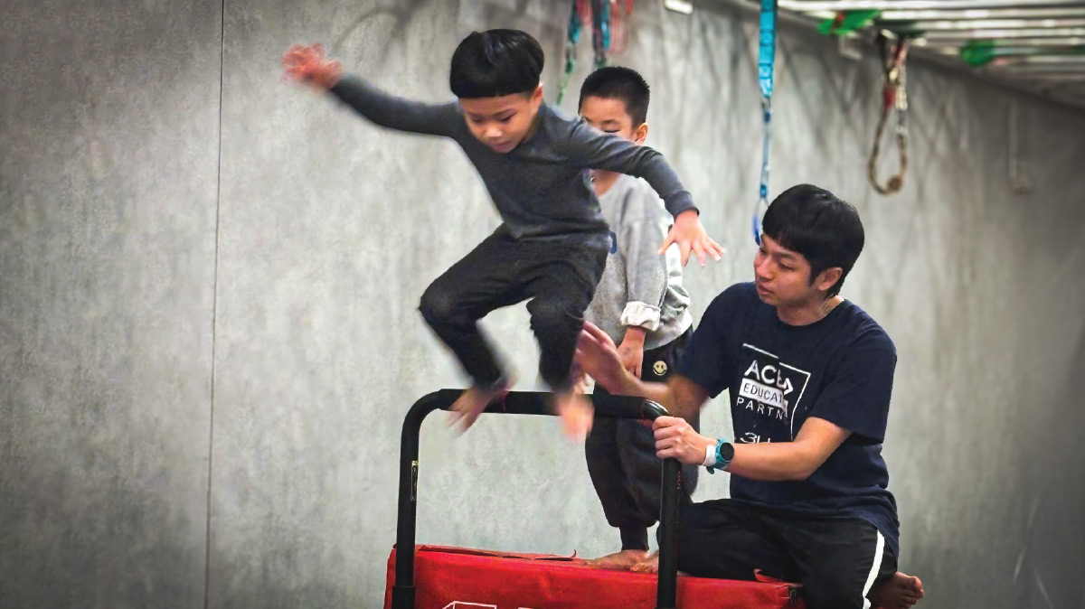 男孩在專業老師保護下進行障礙跳躍練習，訓練下肢爆發力 (Power) 與落地緩衝技巧，提升身體協調性與動作控制 (Motor Control) 能力。