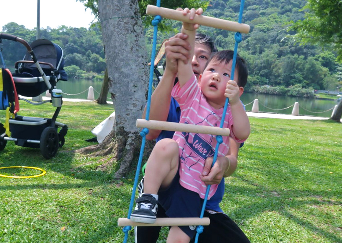 幼兒在戶外自然環境中挑戰軟式繩梯攀爬，這項活動能強化上肢肌耐力與抓握力，並透過克服高度恐懼建立自信心與冒險精神。