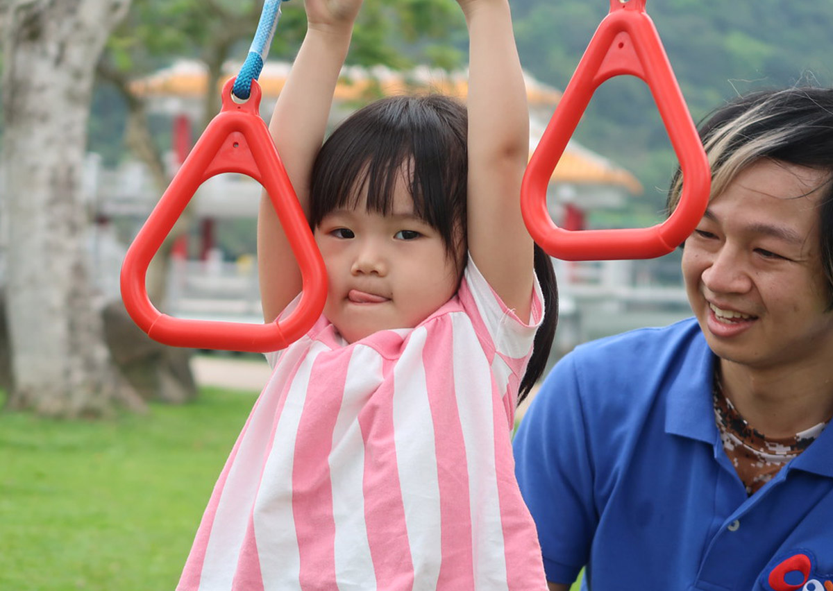 女童在戶外展現堅毅表情進行吊環懸吊，這不僅訓練手部小肌肉與肌耐力，更透過戶外教育培養孩子面對挑戰不放棄的心理韌性 (Resilience)。