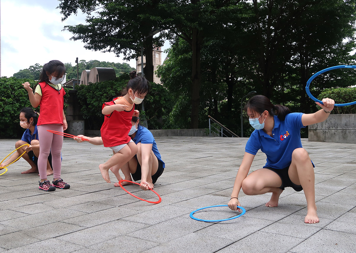 兒童在戶外廣場進行連續跳圈圈遊戲，訓練雙腳起跳技巧與下肢爆發力 (Lower Limb Power)，並透過戶外空間提升對距離與深度的視覺判斷。