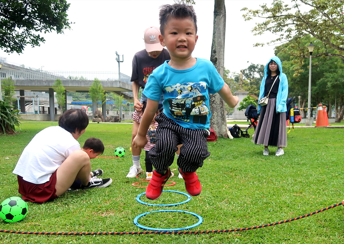 男童在戶外公園進行連續跳圈圈練習，訓練雙腳起跳的協調性與下肢爆發力，並在自然環境中提升對距離感的視覺判斷。