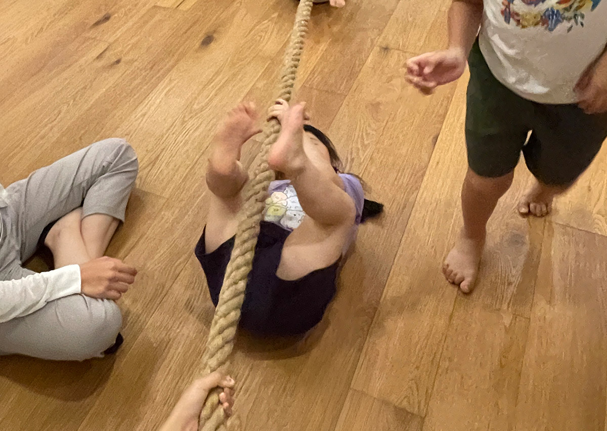 兒童以仰臥姿勢抓握繩索前進，這項特殊的體能動作專注於訓練背部後側鏈 (Posterior Chain) 肌群與手部抓握力，有助於改善駝背並增強全身協調。