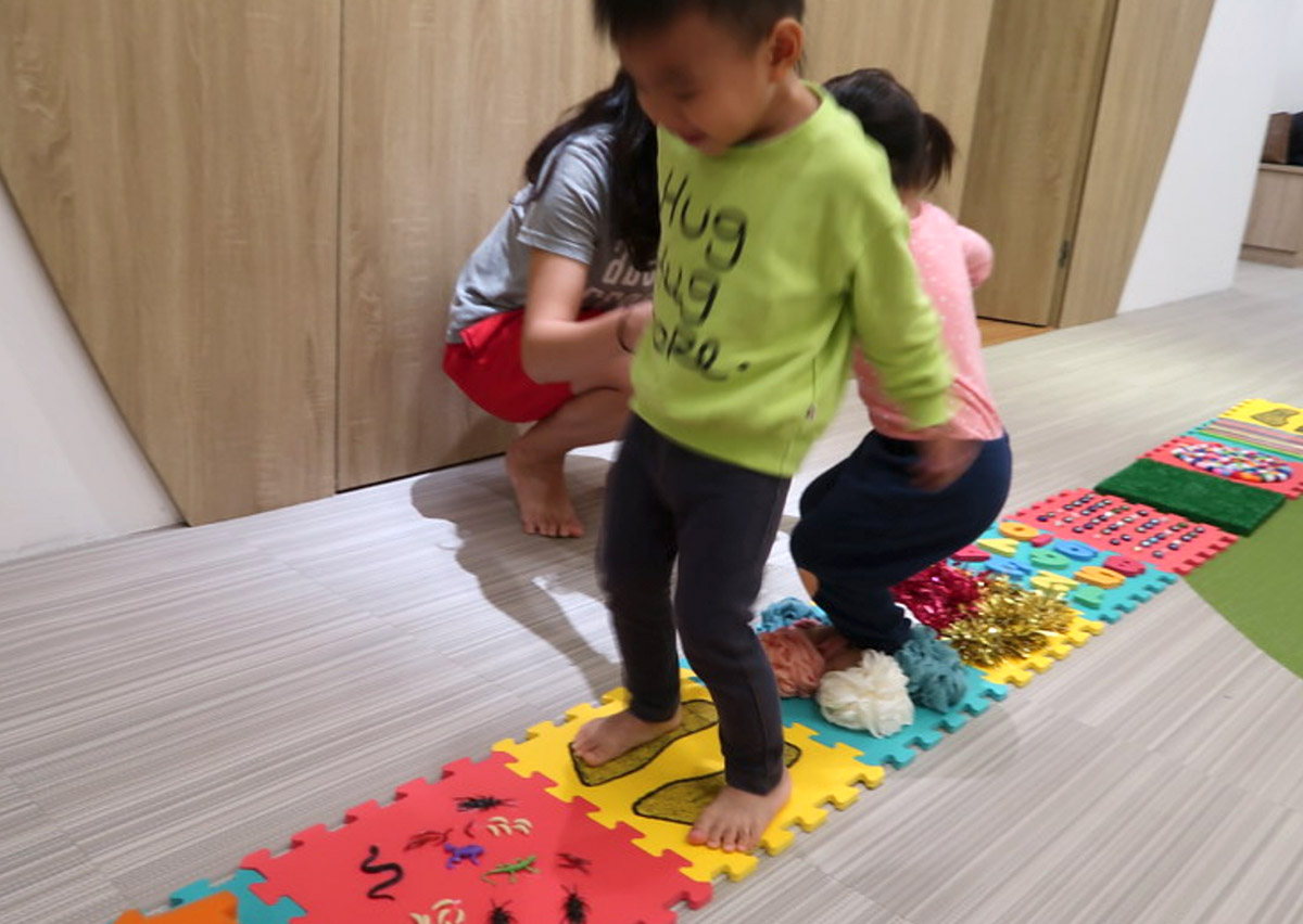 幼兒赤腳行走於不同紋理的觸覺步道 (Sensory Path)，這項感統訓練能直接刺激足底神經，促進大腦對觸覺的整合能力，並強化行走時的平衡穩定度。