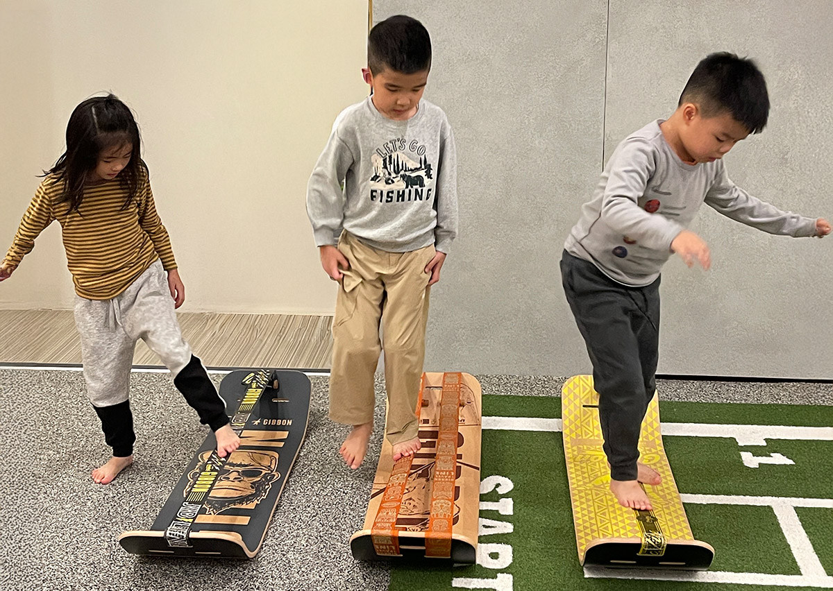 兒童練習站立於不穩定的彎板上，這項訓練能刺激腳底本體感覺 (Proprioception)，強化下肢肌力並矯正姿勢控制，幫助孩子建立穩定的身體軸心。