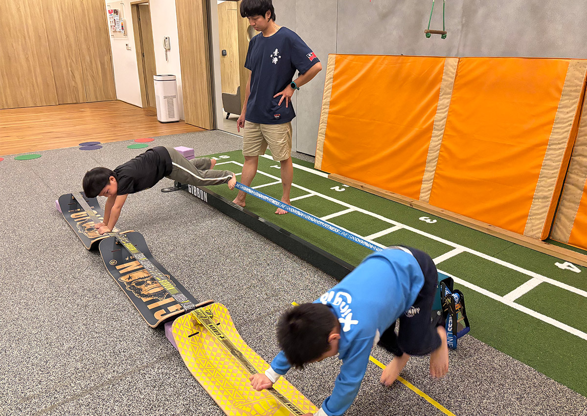 兒童在 Oovi 教練指導下利用彎板 (Slackboard) 進行支撐練習，這項動作能強化核心肌群 (Core Muscles) 與肩帶穩定度，是提升孩子坐姿端正與專注力的基礎訓練。