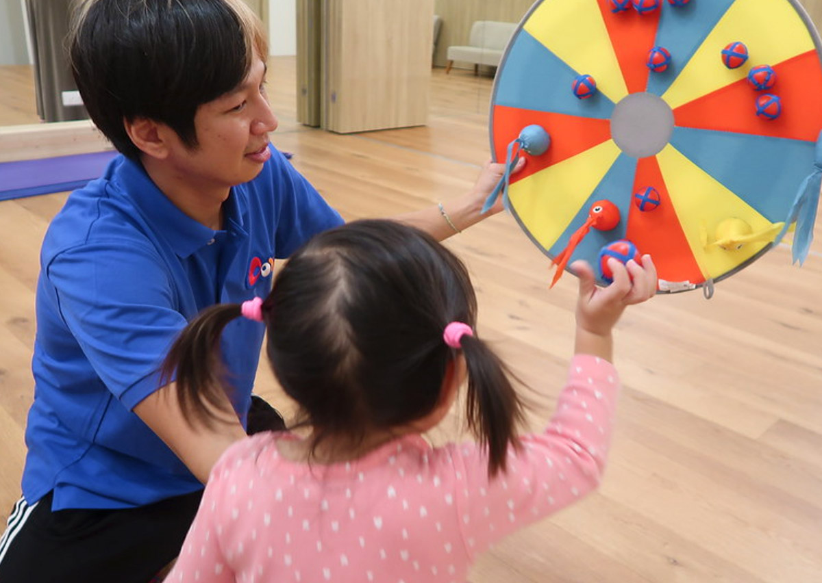 教練引導幼兒使用黏黏球進行標靶投擲，這項精細的目標導向遊戲能訓練孩子長時間的視覺專注力與手部肌肉控制的精準度。
