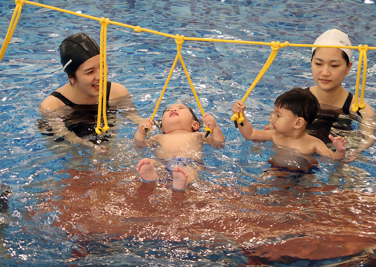 家長輔助幼兒抓握水上懸吊繩索，進行仰漂 (Back Float) 與核心平衡訓練，增進孩子在水中的前庭覺發展與穩定度。