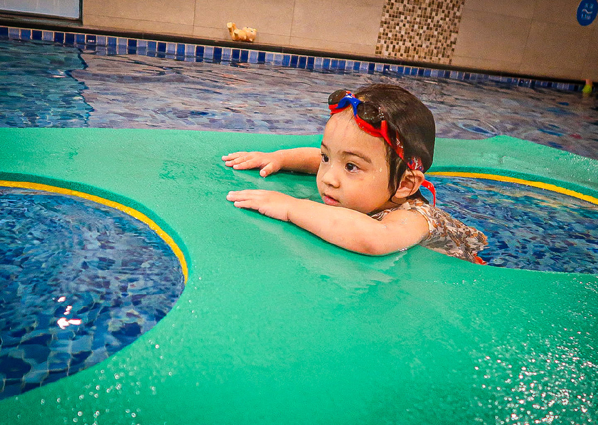 幼兒練習攀附於大型浮毯邊緣，模擬岸邊攀爬 (Wall Climbing) 自救技巧，訓練手臂肌肉力量與水中生存能力 (Survival Skills)。