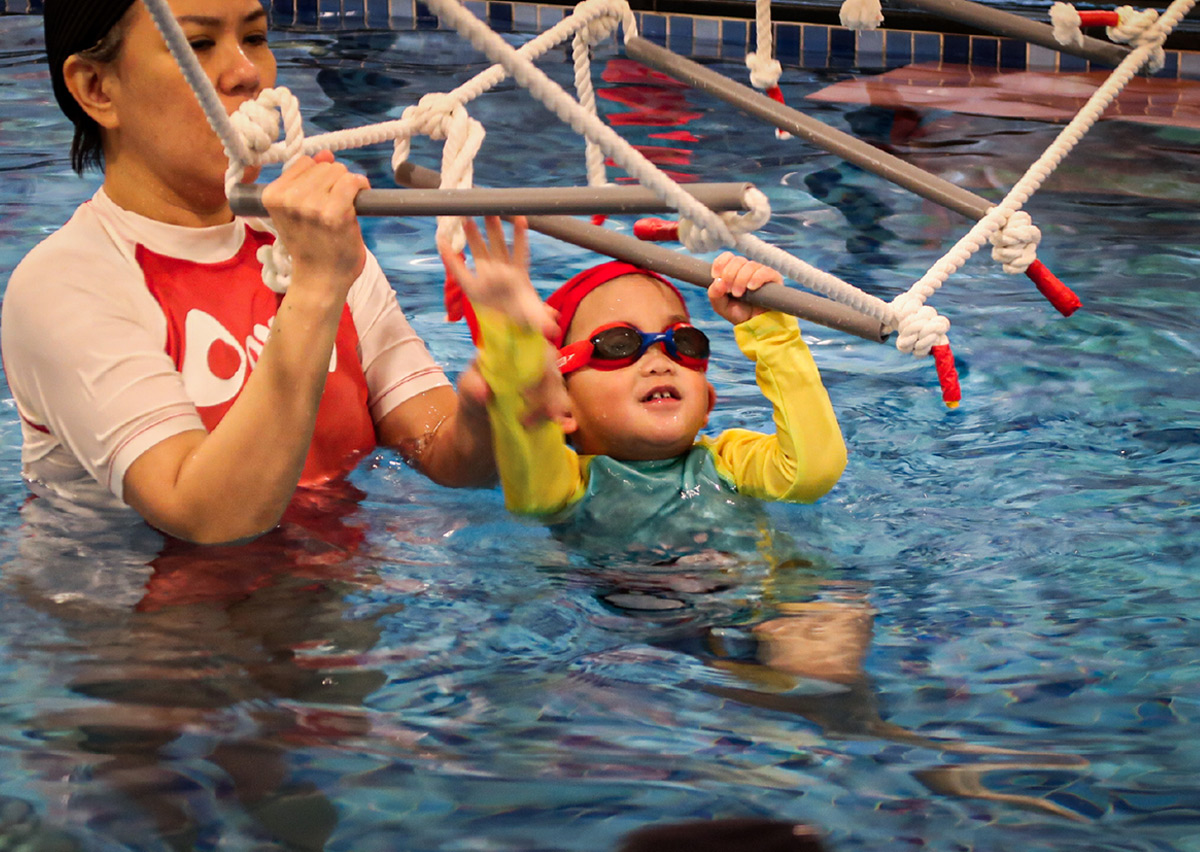 專業教練指導幼兒抓握水上monkey bar，訓練上肢肌力與手眼協調，將體操元素融入游泳教學中，提升大肌肉發展。