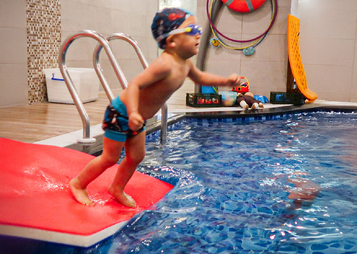 幼兒自信地從岸邊跳入水中，練習安全入水 (Safe Entry) 姿勢與入水後的閉氣反應，培養水中膽量與自信心。