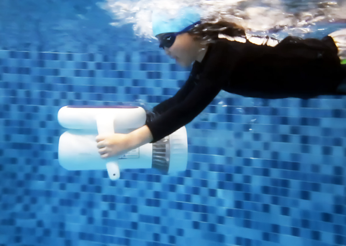 兒童佩戴泳鏡在水中操作白色的水中推進器 (Underwater Scooter) 進行潛水推進練習,這項結合科技的創新課程能強化學員的身體流線控制 (Streamline Control) 並激發對水上運動的深層興趣。