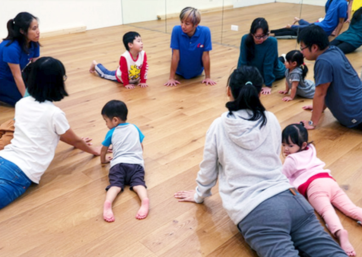 老師帶領兒童圍圈進行兒童瑜珈 (Kids Yoga) 的眼鏡蛇式伸展，透過動作模仿訓練背部肌群與核心力量，並在靜態活動中培養孩子的情緒穩定與專注力。