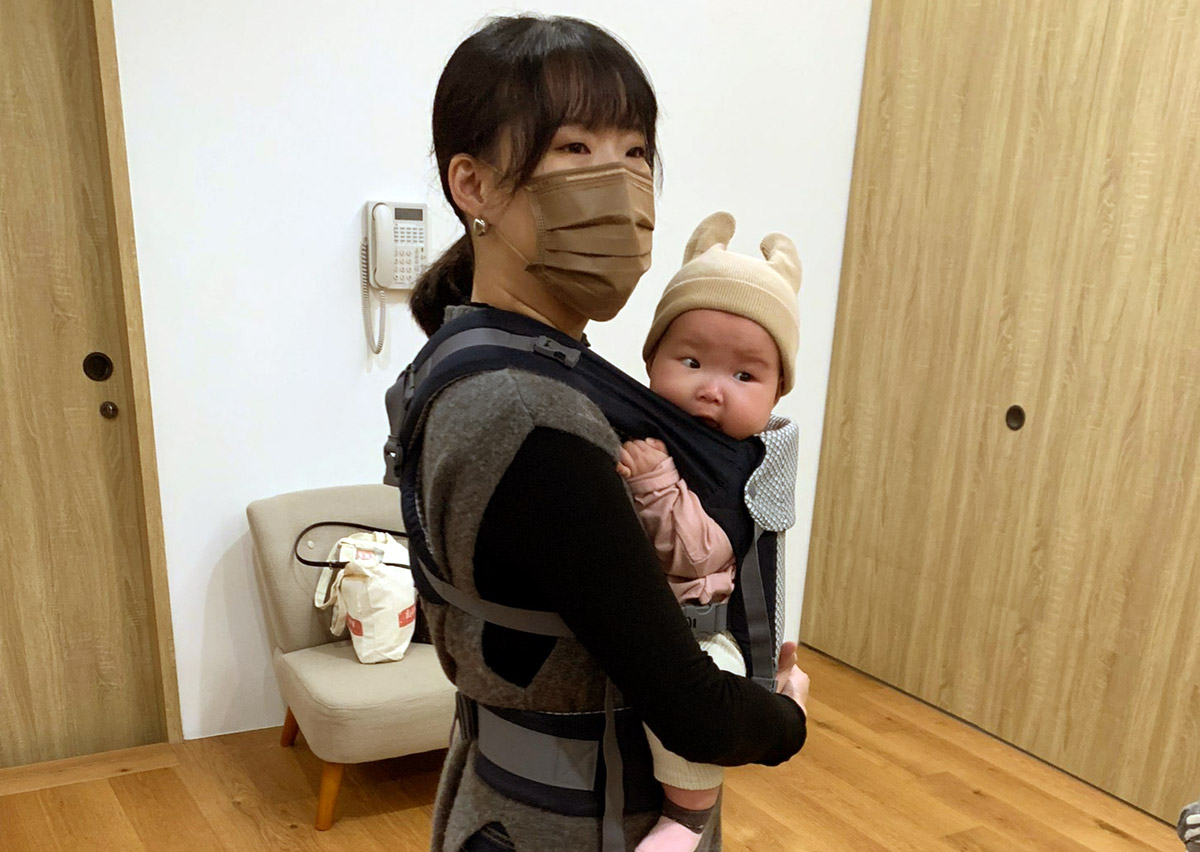 媽媽示範揹巾穿戴後的安全檢查重點，確保寶寶頭部貼近親吻距離 (Close enough to kiss) 且呼吸道暢通，展現正確穿戴對於預防嬰兒髖關節發育不良 (DDH) 的重要性。