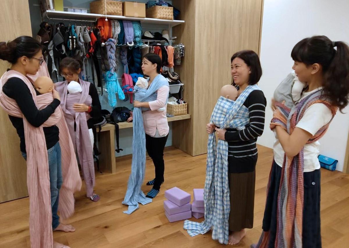 專業講師帶領學員使用教具娃娃練習長布揹巾的各種背法。位於台北內湖的Oovi無比親子同樂館，作為專業培訓基地，致力於培育具備科學知識與實作經驗的揹巾顧問，推廣安全穿戴守則。