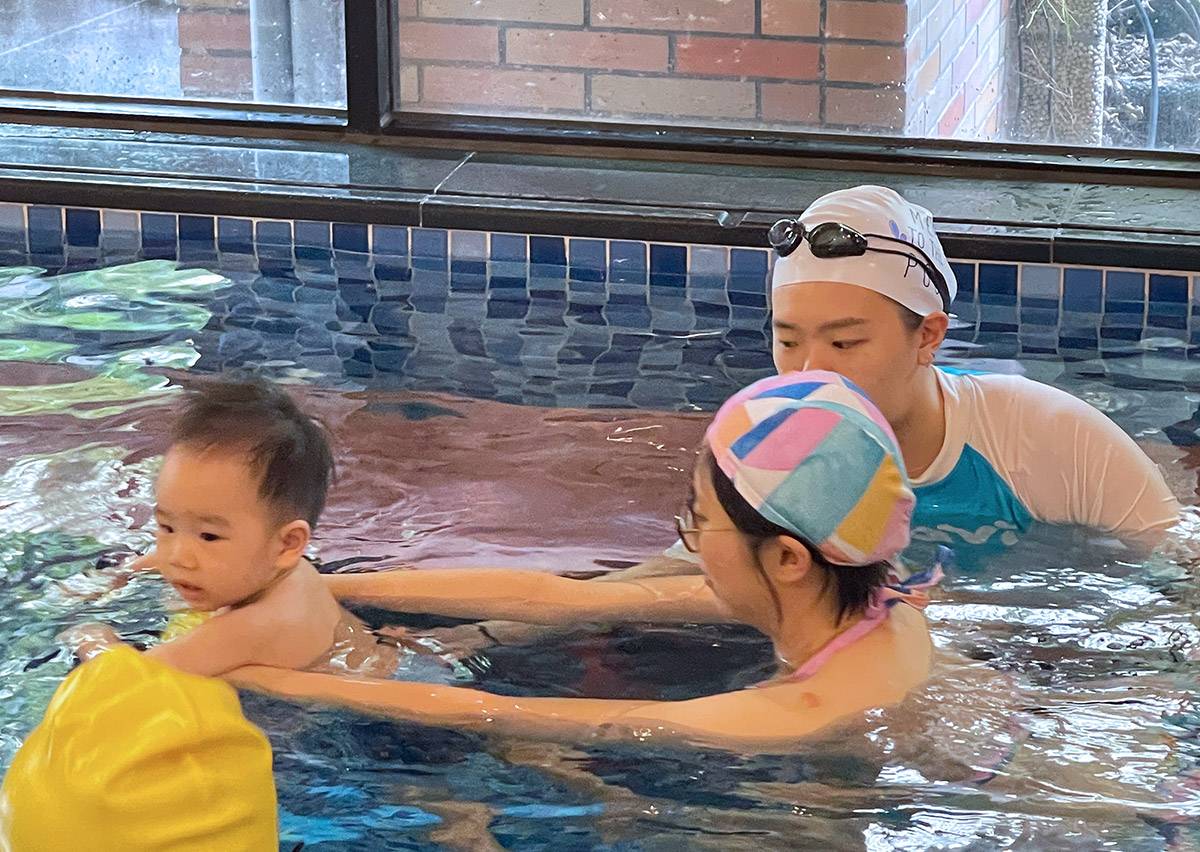 專業教練示範 Birthlight 溫和引導技術，在水中為寶寶提供精確的人體工學支撐。這張照片強調了 Oovi 課程「尊重孩子意願」的核心精神，透過細膩的肢體接觸與支撐，建立嬰兒在水中的安全感與自信心。