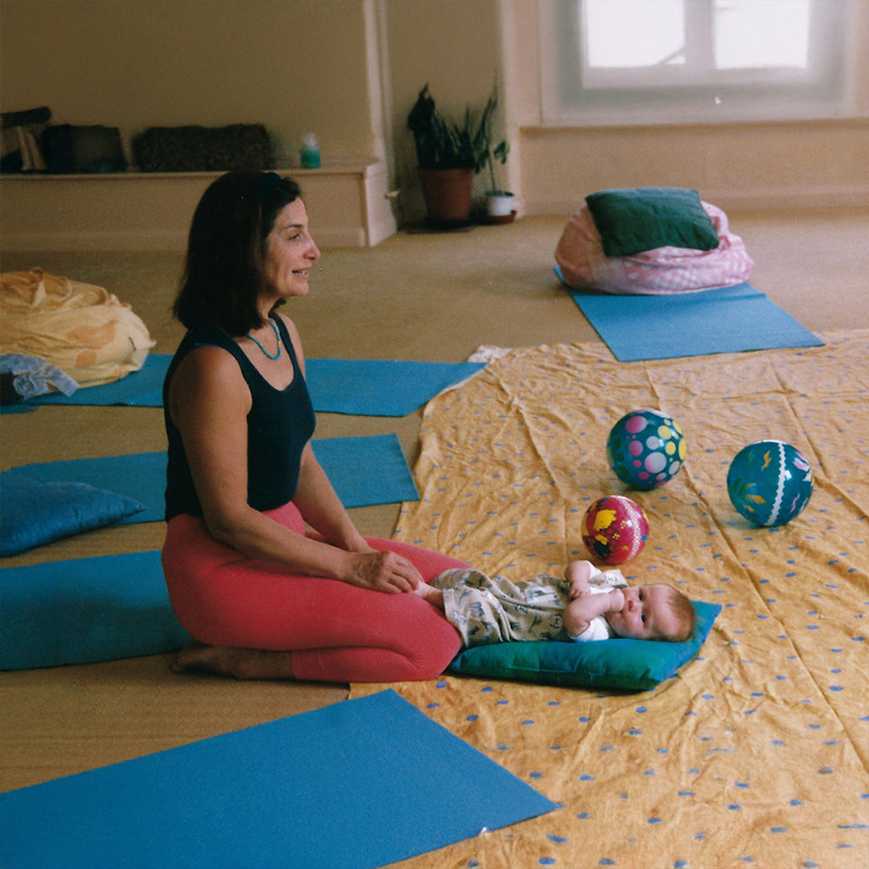創辦人 Françoise Freedman 於室內教室示範嬰兒瑜珈 (Infant Yoga) 的基礎動作。這項專業培訓結合了肢體拉伸與感官啟蒙，旨在促進嬰幼兒的大肌肉發展，並協助產後媽媽達成身心修復與親密育兒目標。
