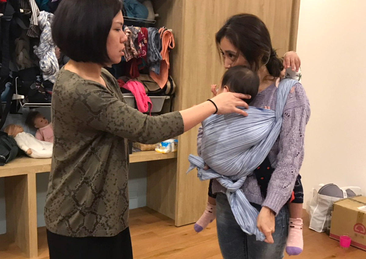 Oovi 專業顧問一對一協助媽媽調整長布揹巾 (Woven Wrap) 的布料張力，確保寶寶脊椎呈現健康的 C型背，並透過分段拉緊技巧解決產後媽媽腰痠背痛的問題。