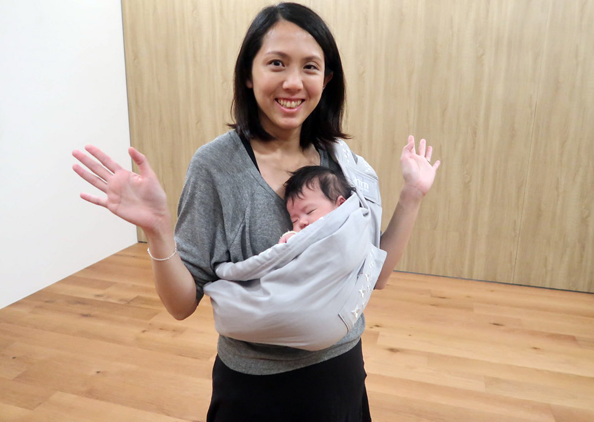 媽媽使用單肩揹巾攜帶熟睡寶寶，自信張開雙手展示解放雙手 (Hands-free) 的便利性，證明合適的揹巾能讓家長在安撫高需求寶寶的同時，保有生活行動力。