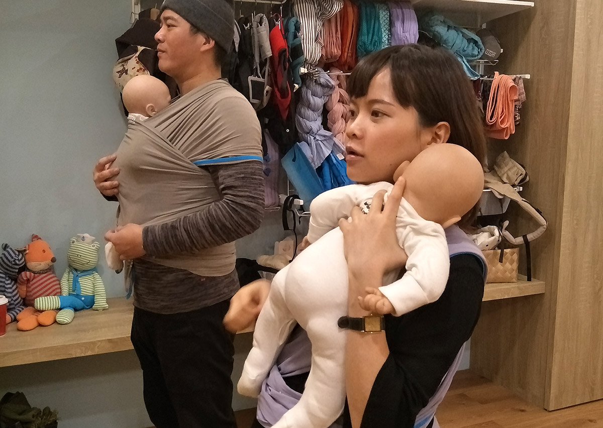 課堂上爸爸與媽媽分別使用長布揹巾與專業負重娃娃進行操作練習。Oovi 顧問透過模擬實作幫助家長建立肌肉記憶，消除面對真寶寶操作時的緊張感。