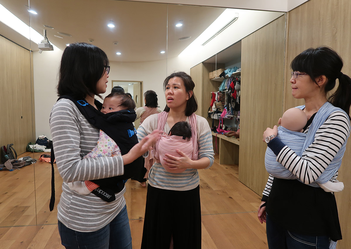 學員們在 Oovi 教室透過大鏡子檢視揹巾穿戴細節，學習觀察寶寶姿勢與布料張力，這種視覺回饋 (Visual Feedback) 與團體互助的學習模式，能大幅提升家長操作的準確度與自信心。
