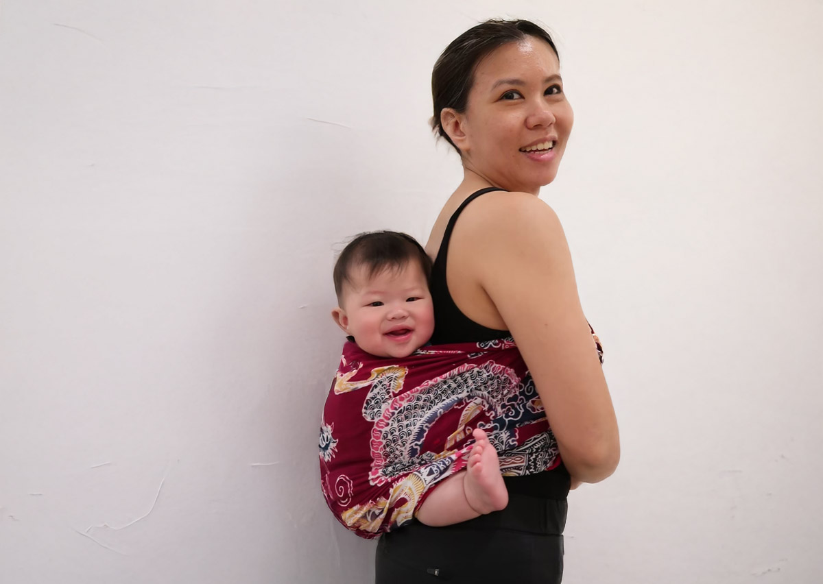 媽媽自信展示紅色圖騰的編織長布揹巾 (Woven Wrap)，呈現揹巾穿戴不僅符合人體工學舒適度，更能成為展現家長個人風格的時尚配件，打破育兒用品單調的刻板印象。