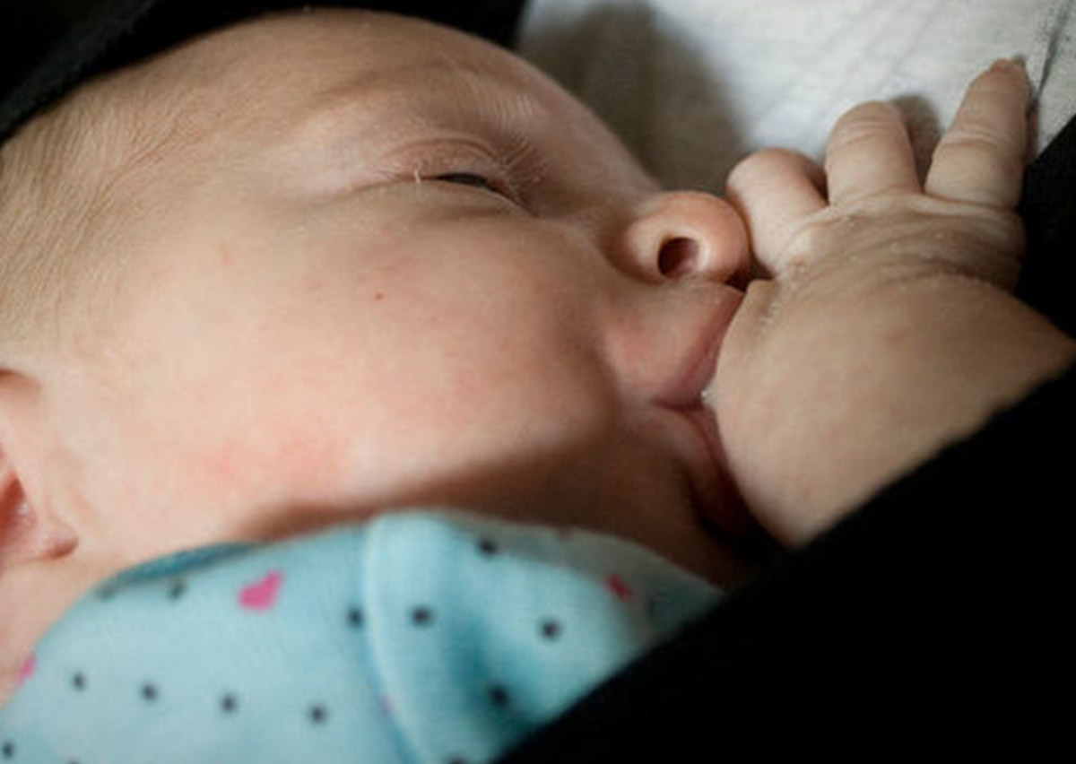 捕捉寶寶在揹巾內親餵母乳 (Breastfeeding in Carrier) 的特寫畫面，展示揹巾穿戴提供的極佳隱密性與便利性，支持母乳媽媽達成隨需哺餵 (Feeding on demand) 的育兒目標。