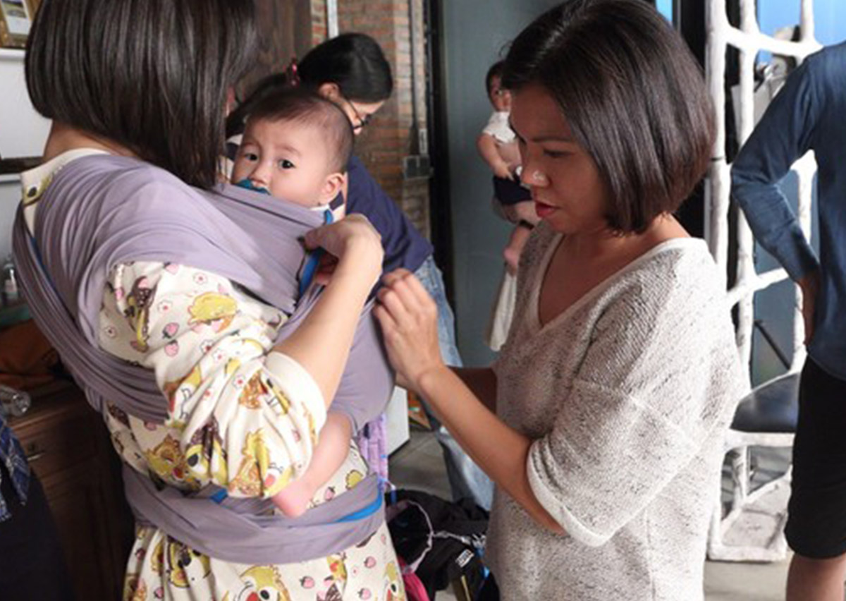 顧問細心協助媽媽調整灰色長布揹巾的頸部支撐 (Neck Support)，確保新生兒頭部穩定且呼吸道暢通，嚴格遵守 T.I.C.K.S. 安全穿戴守則。