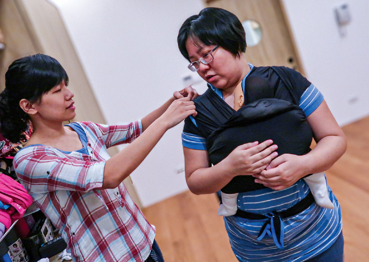 顧問指導媽媽調整彈性揹巾的肩部支撐點，強調受力均勻的重要性，透過專業調整預防家長常見的肩頸痠痛，確保長途揹負時的人體工學舒適性。