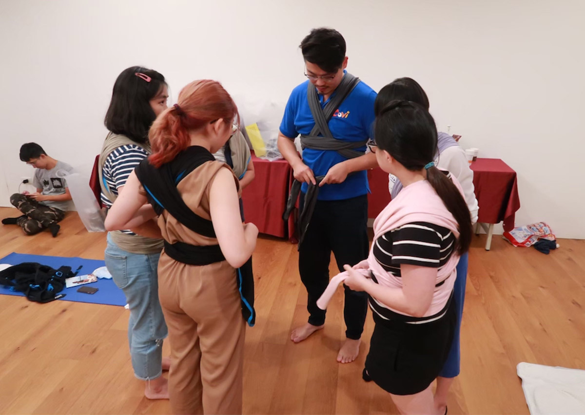 講師示範如何引導家長操作複雜的揹法，強調教練在教學過程中「手部引導」與「口語指令」的精確性，提升親職教育的溝通效能。