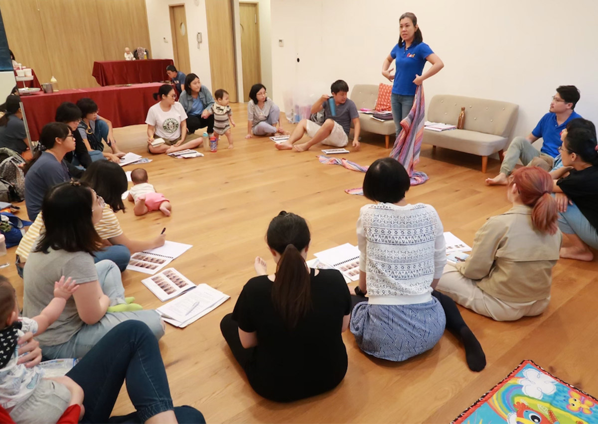 講師在圓圈討論中示範揹巾的操作重點，展示參與式教學如何讓每位學員都能清楚觀察細節，增進團體互動與學習動力。