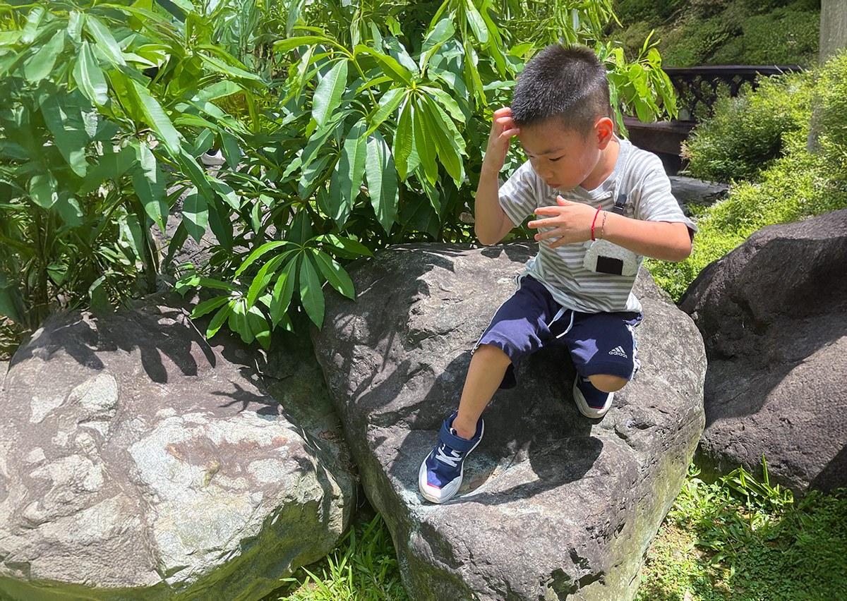 孩童在戶外石群上練習攀爬跳躍，透過直接接觸自然質地強化觸覺感知、平衡感與環境適應力。