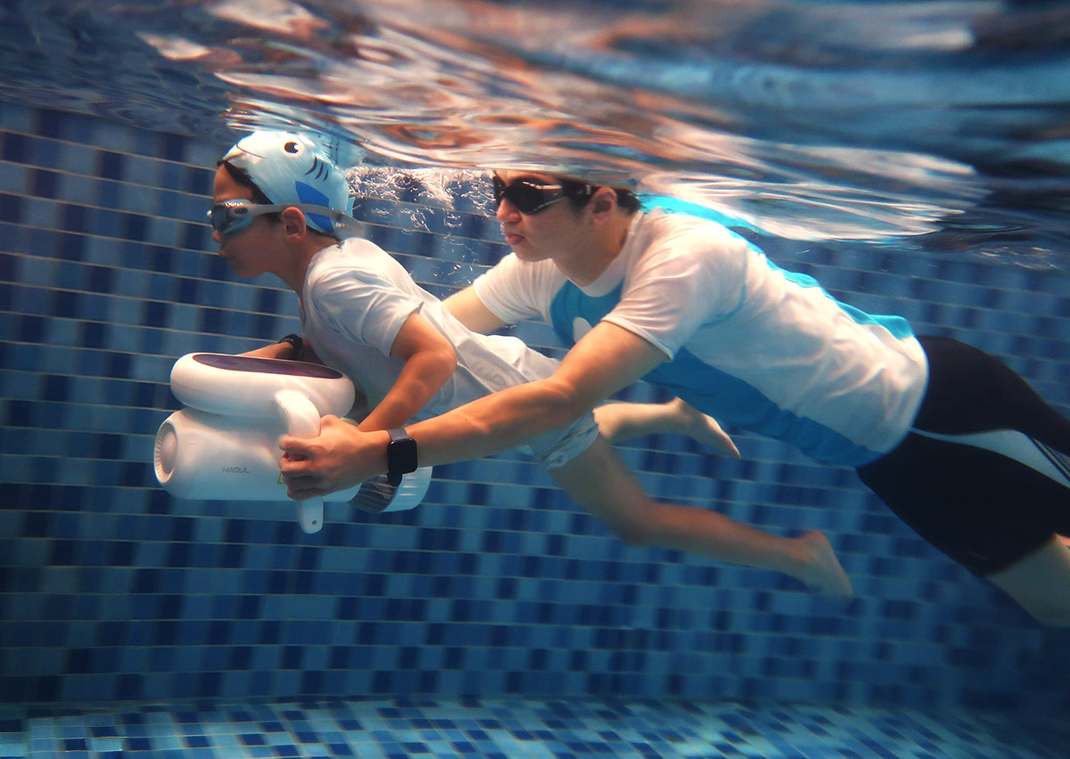 專業教練在水下近距離輔助孩童使用推進器，確保操作安全並引導正確的水底導航方向與姿態。