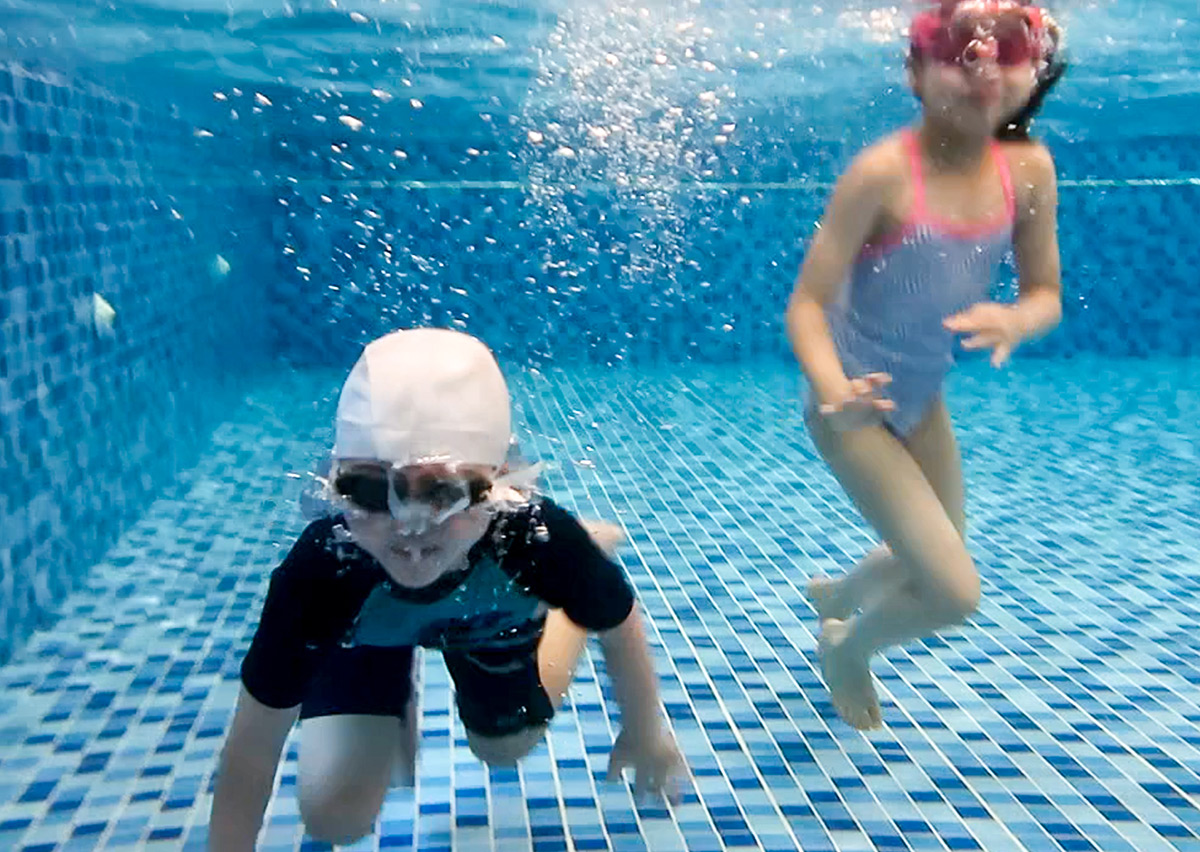 兩名戴著泳鏡的孩童在清澈的泳池底練習潛水，展現優異的水下續航力與自然流暢的水感探索。