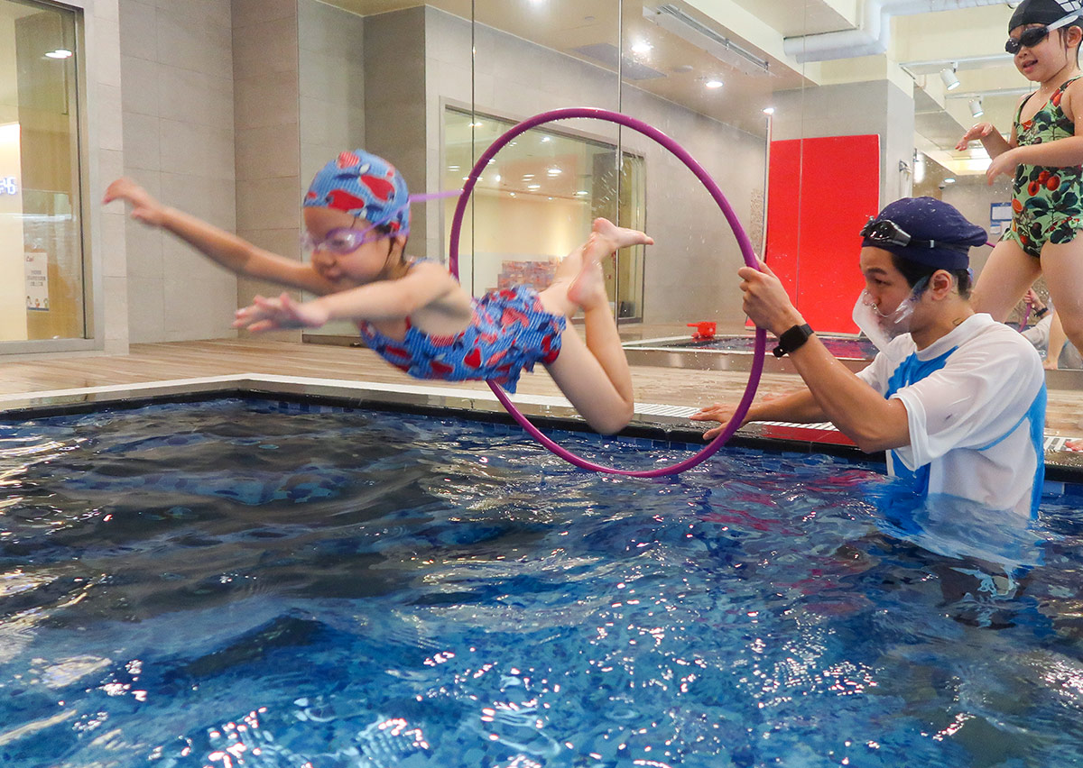 Oovi 暑假營隊學員在教練守護下，精準躍過水中圓環障礙，透過挑戰遊戲提升空間判斷力與水域勇氣。