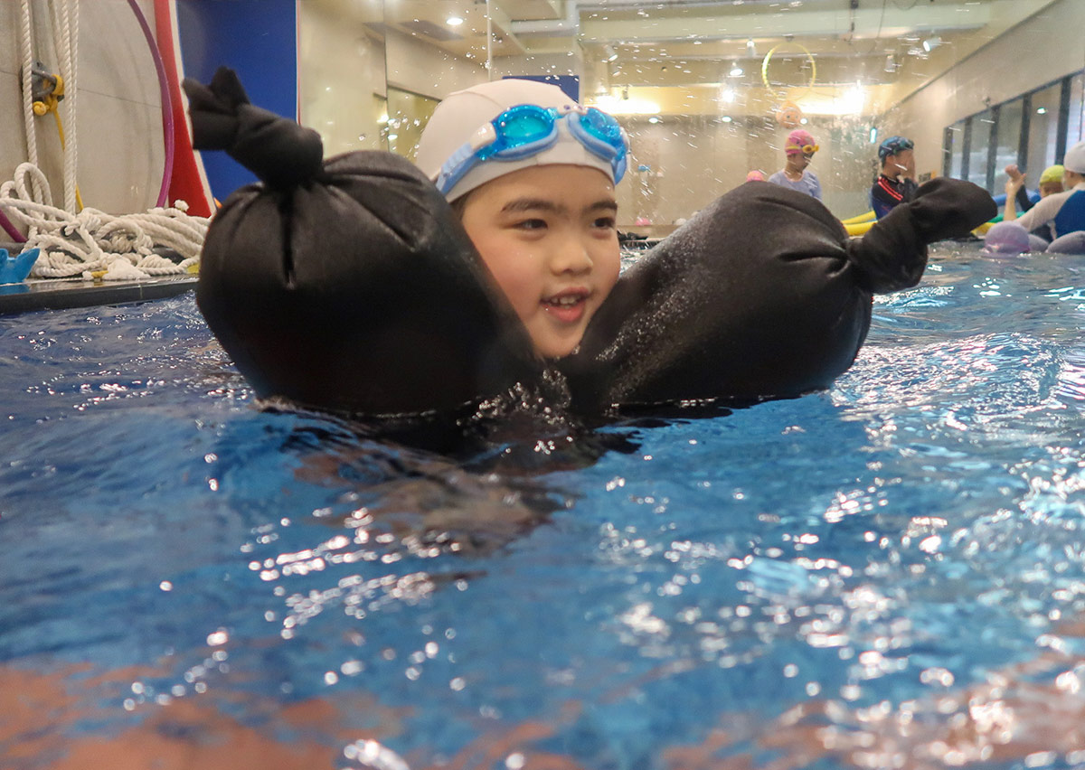 孩童在 Oovi 營隊中練習使用充氣救生包維持水面漂浮，透過模擬情境強化水域安全意識與應變能力。