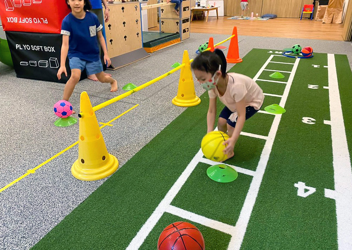 Oovi 暑假營隊學員在室內運動場進行球類運送挑戰，結合角錐障礙跑提升手眼協調與肢體反應力。